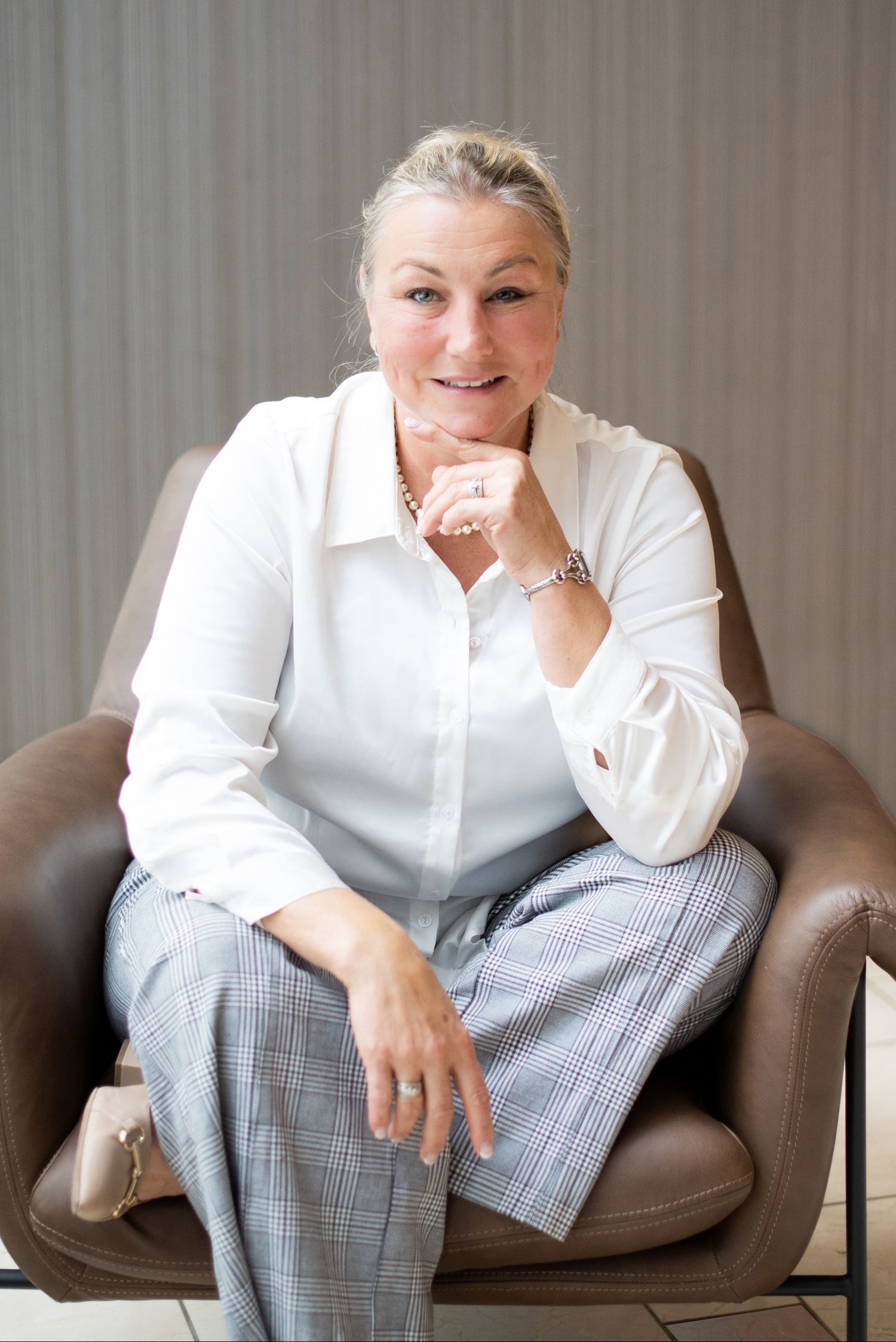 Helena Smrcek sitting in a chair wearing a white blouse and plaid pants, with a neutral background.
